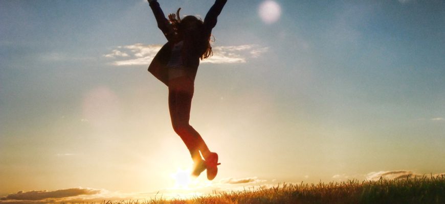 A person jumping in the air, arms extended, against the sunlight.