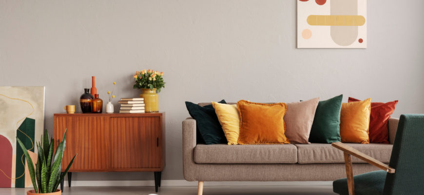 Abstract painting on grey wall of retro living room interior with beige sofa with pillows, vintage dark green armchair and yellow pouf with book