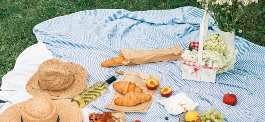 A picnic set up in grass on a blanket with berries, bread, pastries, and flowers