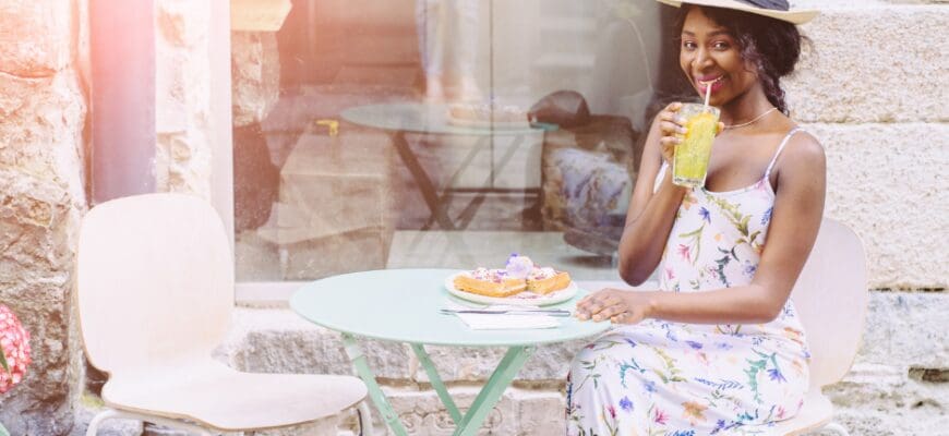 A woman sitting at an outdoor cafe table with a coffee and a plate with a pastry