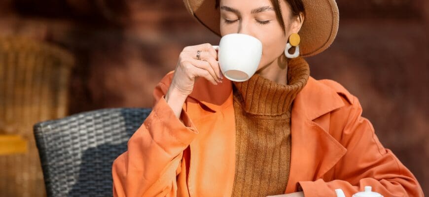 A woman sitting in an outdoor cafe sipping from a mug